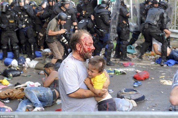 Cảnh hỗn loạn ở biên giới Hungary khi những người tị nạn tại các nước có chiến tranh ào ạt tràn vào biên giới. Trong ảnh là một người đàn ông khuôn mặt đẫm máu vẫn cố gắng ôm lấy bé trai trong lòng. Bé trai đang rất hoảng sợ trước cảnh tượng đẫm máu đang diễn ra.